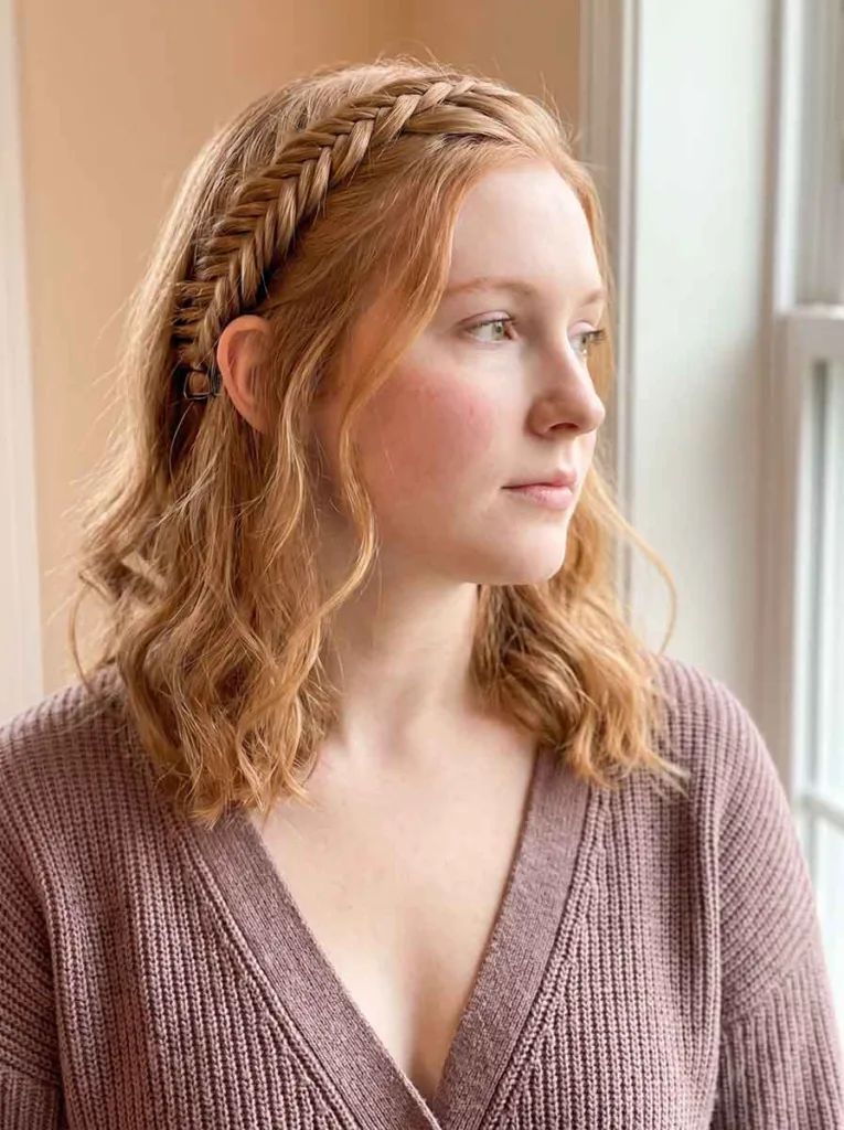22-year-old woman with loose hair and a single accent fishtail braid pinned behind the ear, photographed at a close front angle
