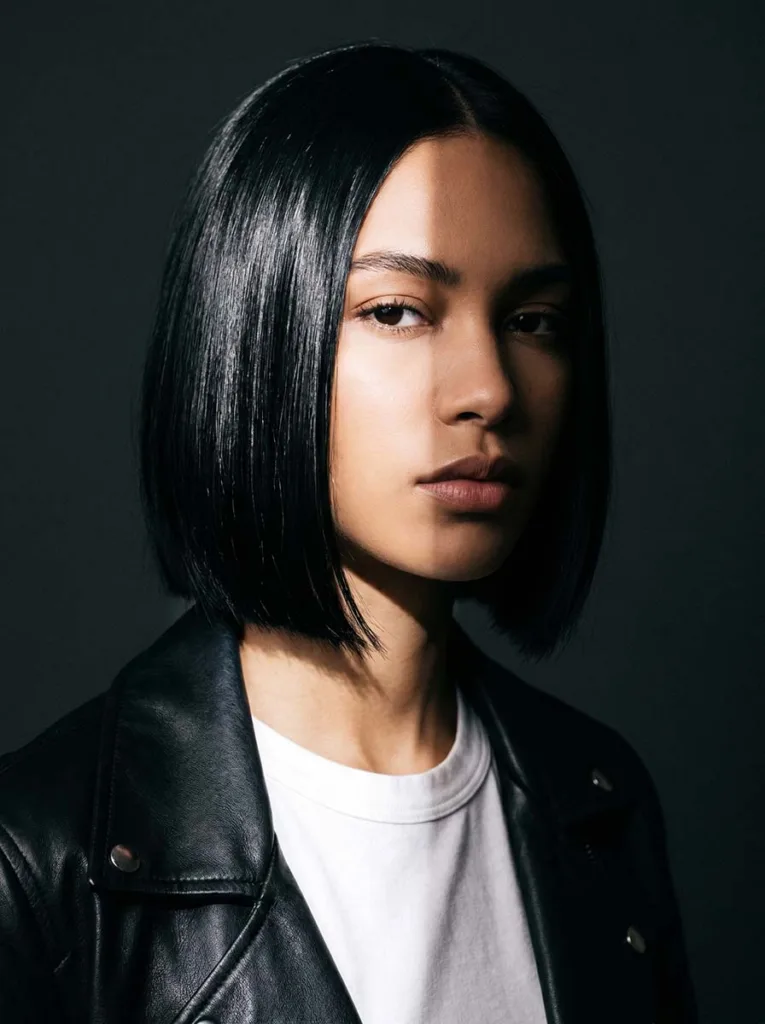 all-over dark onyx glass bob on biracial woman, near-mirror shine, black leather jacket, charcoal background, split lighting