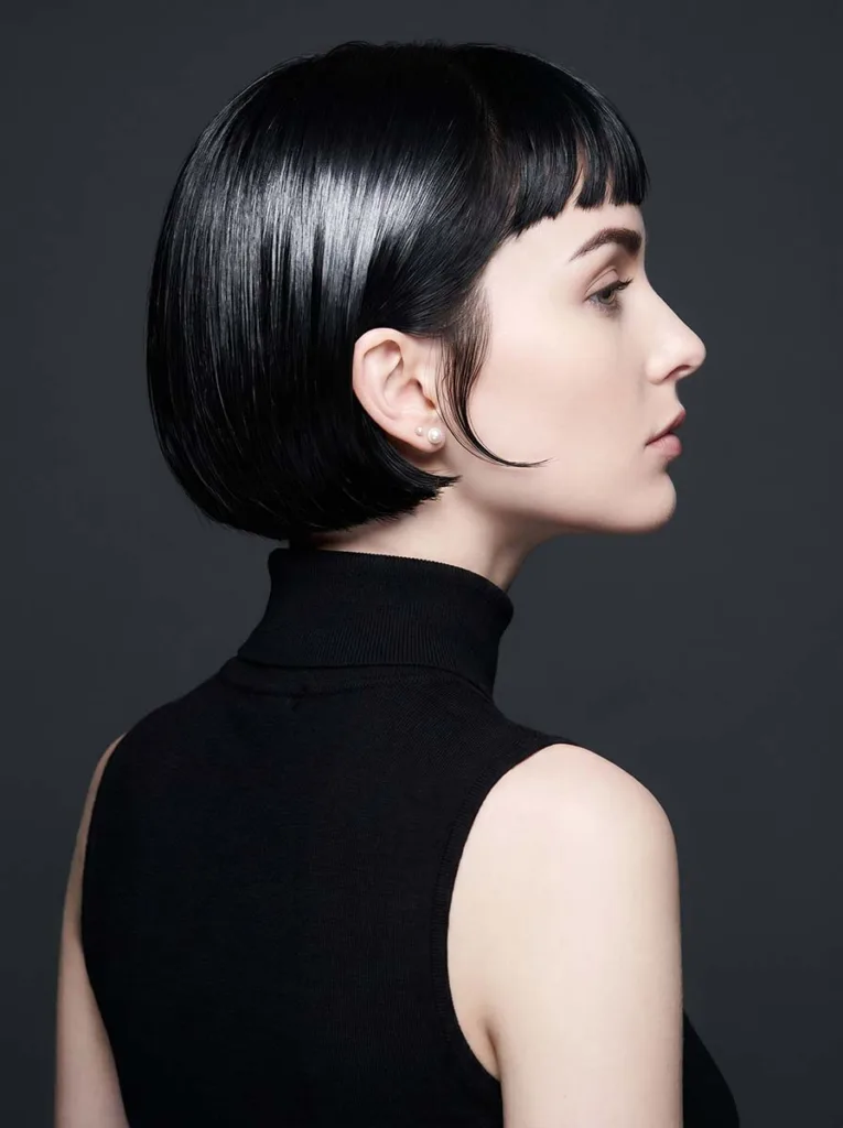 Stunning model with a flawless French bob and sharp baby bangs, glossy jet-black hair, rear three-quarter editorial portrait