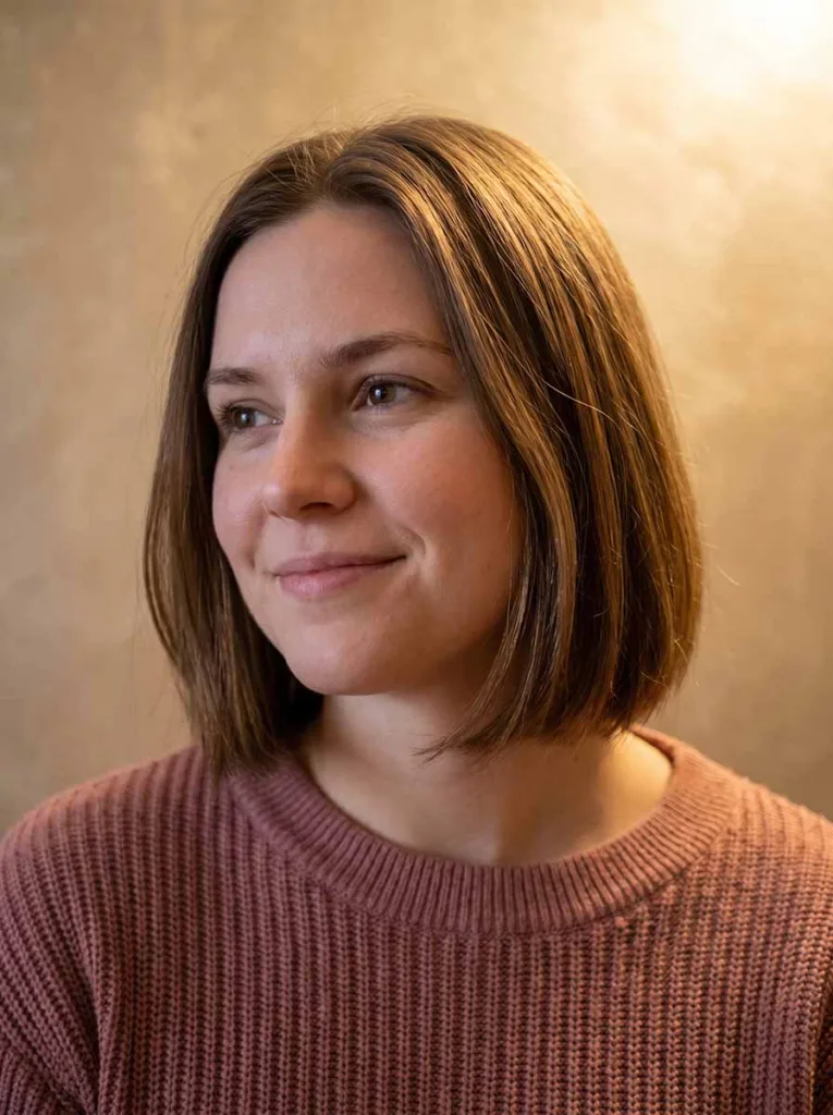 chin-length glass bob on white European woman, medium brown hair, dusty rose sweater, warm champagne gold background