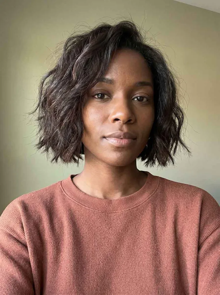 Woman with a choppy short wavy bob above the jaw, razored ends and tousled texture on thick dark hair