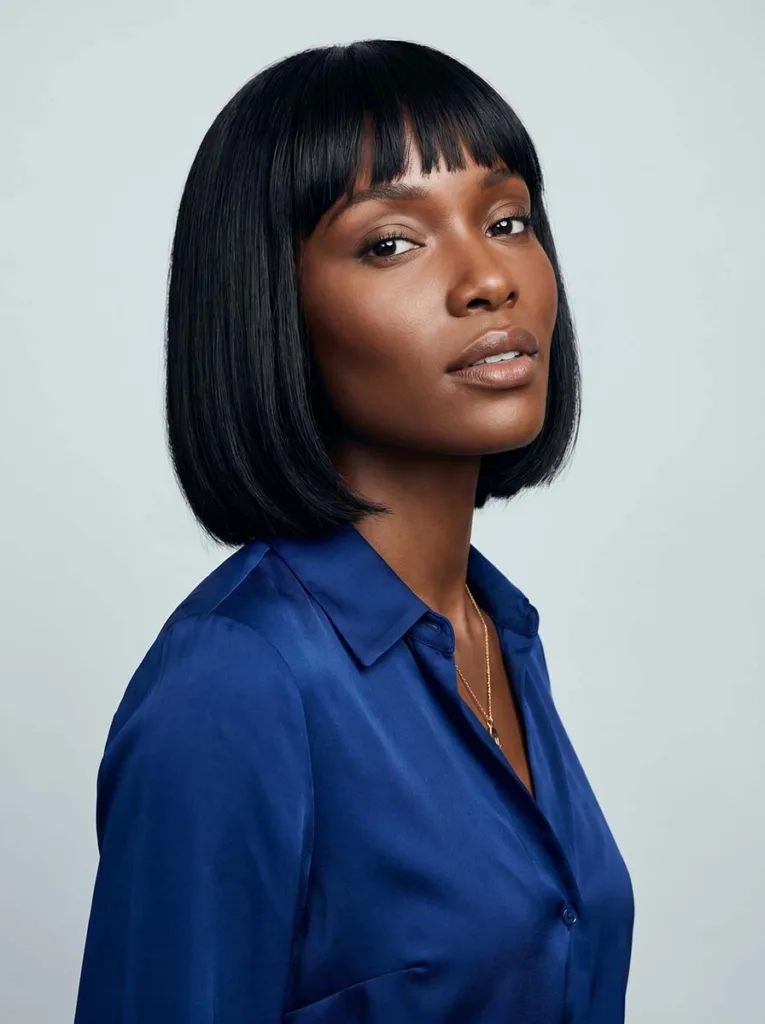 Beautiful model with classic straight blunt baby bangs, glossy black bob, radiant deep brown skin, straight-on editorial studio portrait