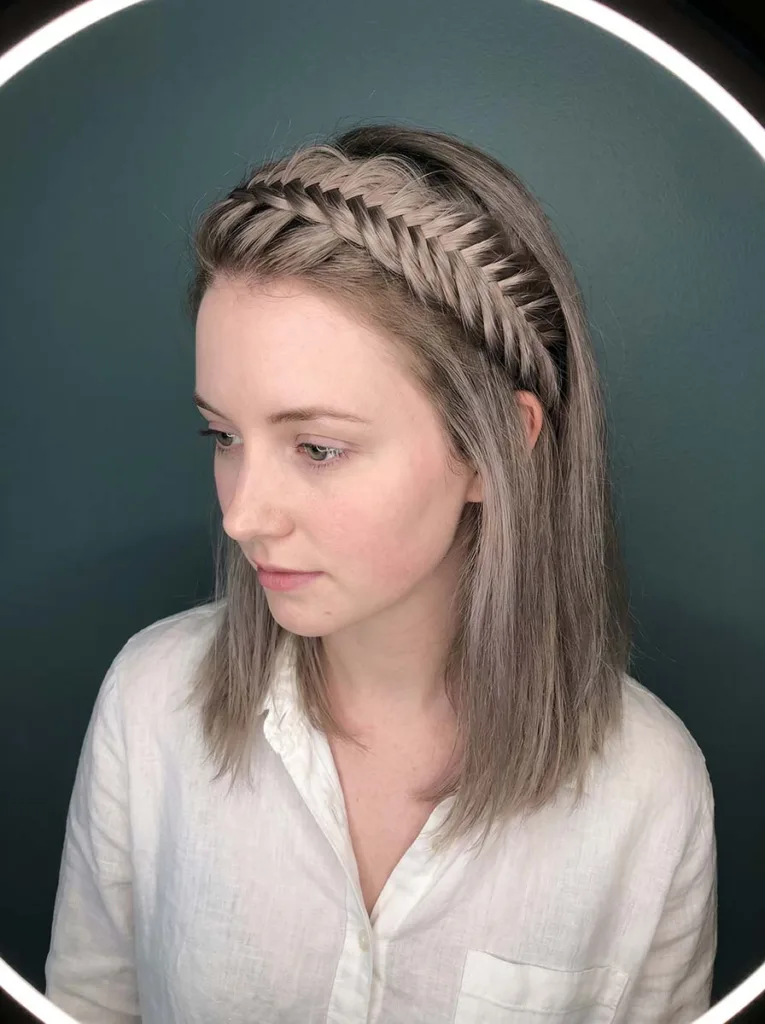 Elevated 3/4 front shot of a young woman with a crown fishtail braid halo clearly visible across the top of her head, against a teal background