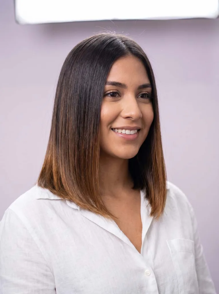 extended glass lob half-body portrait on Latina woman, dark brown to caramel ends, white linen shirt, pale lavender background