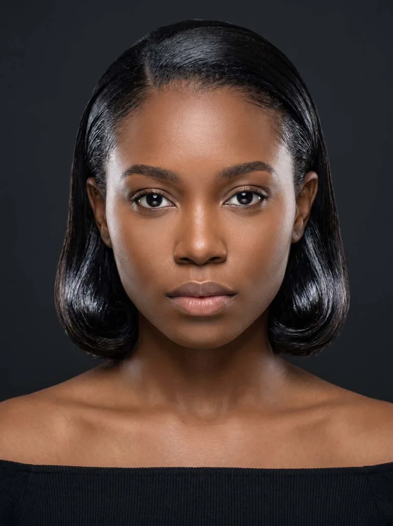 glass bob with slicked-back crown on Black woman, jaw length, glossy free-hanging ends, off-shoulder black top, charcoal background