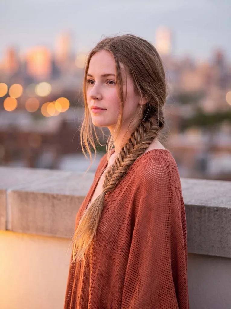 Young woman with a wide, loose boho french fishtail braid wearing a terracotta kaftan at a rooftop setting