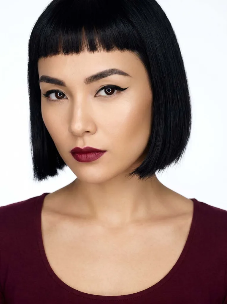 Striking beautiful model with ultra-short micro bangs, sleek jet-black bob, flawless olive skin, extreme close portrait on white