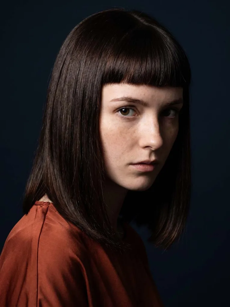 micro bangs glass bob on white woman, espresso dark hair, rust silk top, deep navy background, overhead angle