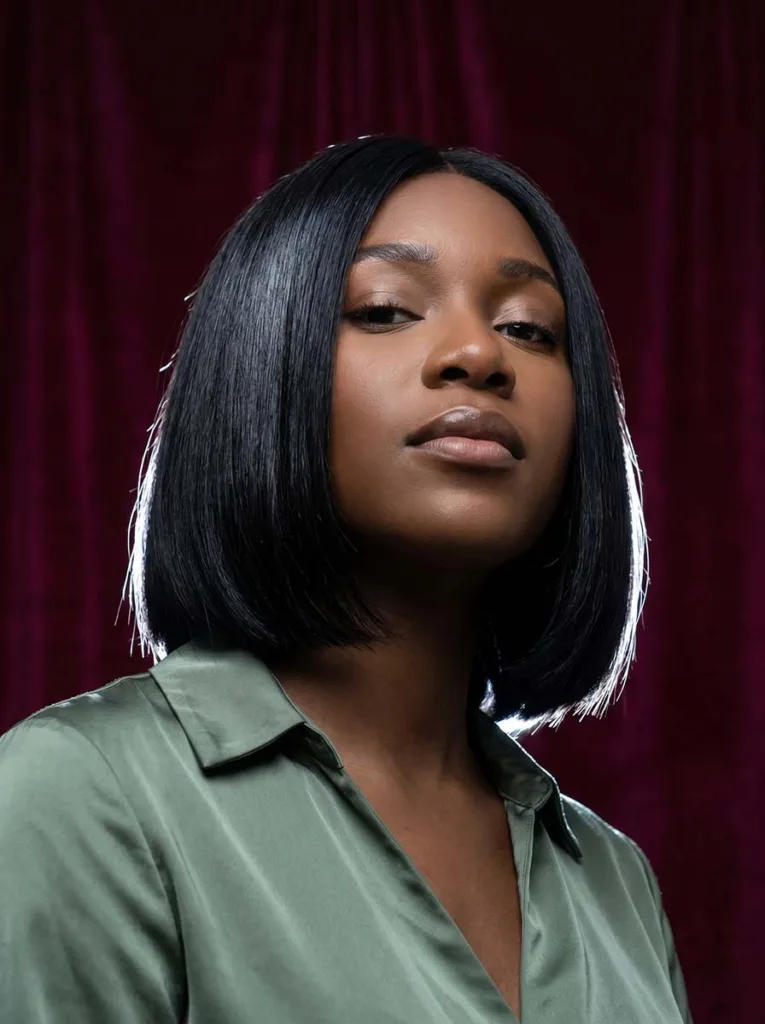 natural black glass bob on Black woman, near-lacquer shine, sage green silk top, burgundy background, dramatic rim lighting