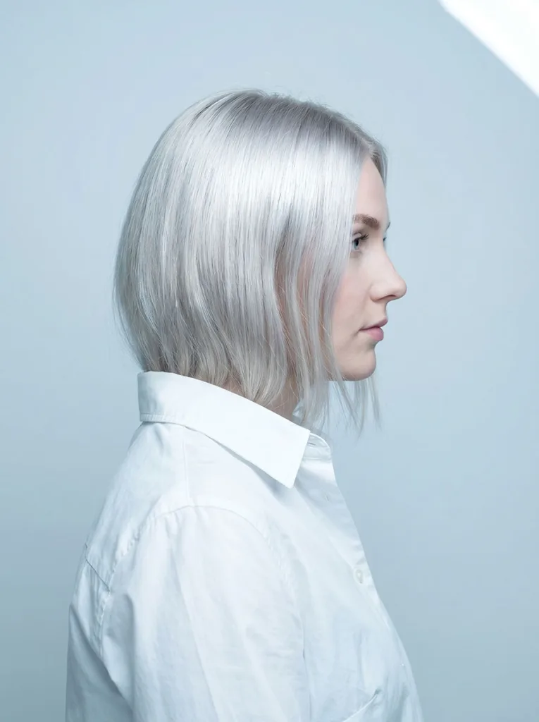 platinum blonde glass bob back three-quarter view, cool silver tones, white button-down, icy blue-grey background