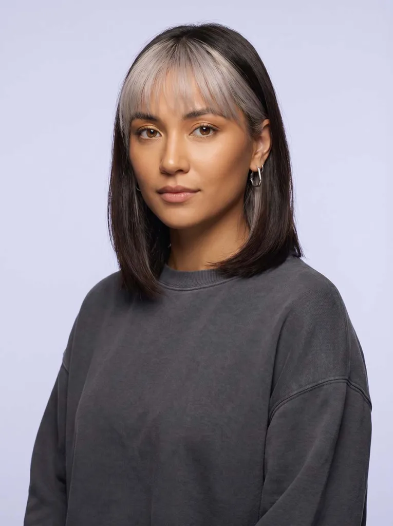 Beautiful model with ice-platinum baby bangs against dark brunette hair, warm golden skin, three-quarter portrait against soft lilac background