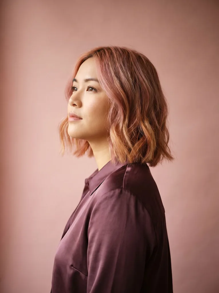 Woman with a rose gold wavy bob, warm pink-blonde waves catching soft studio light