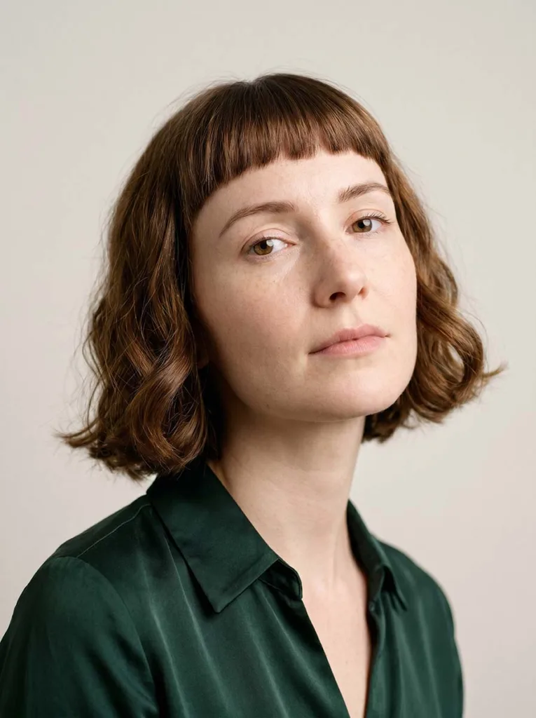 Woman with a short wavy bob and straight-across baby bangs, loose waves framing the face