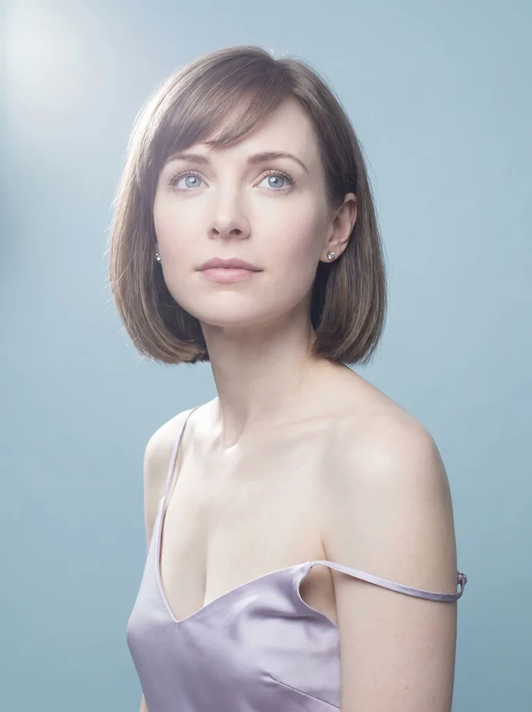 Beautiful model with side-swept baby bangs, ash brown bob, cool elegant features, low-angle close portrait in ice-blue studio
