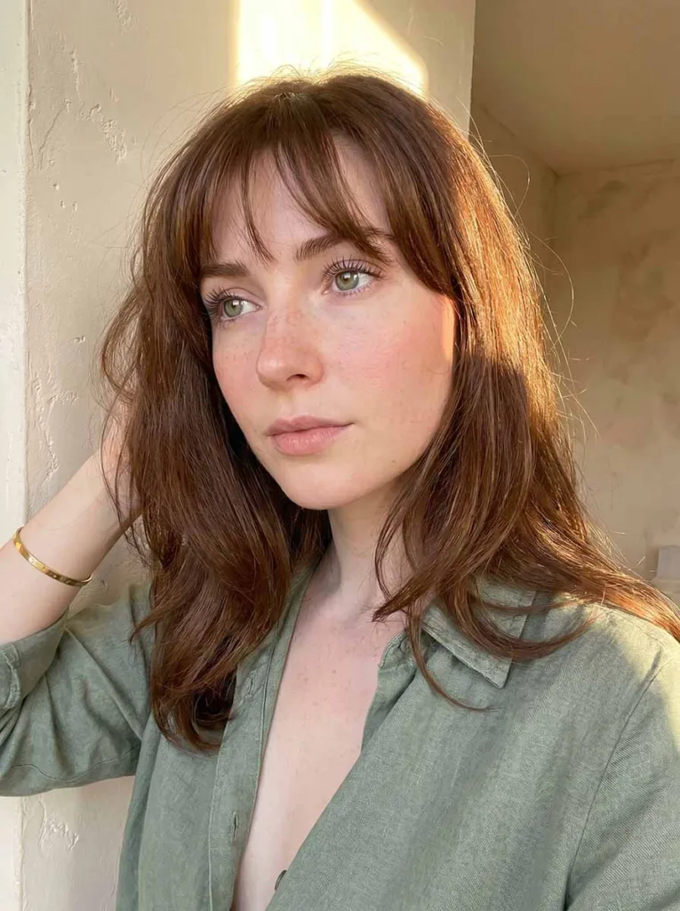 Gorgeous model with wispy feathery baby bangs, glowing fair skin, warm brunette waves, three-quarter portrait in soft afternoon light