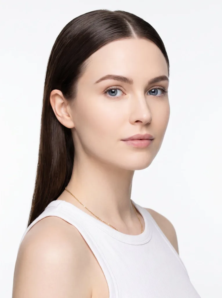 Gorgeous 23-year-old woman with ivory skin and dark chocolate hair in a classic center-part sleek low bun, 3/4 front portrait, white studio background