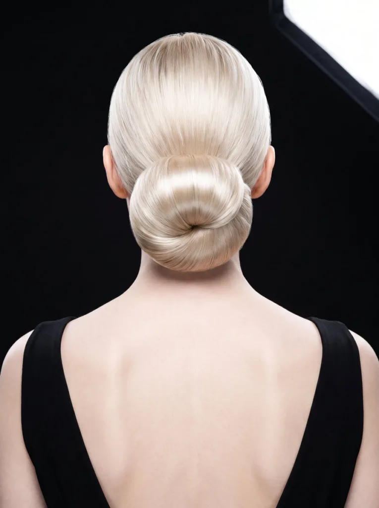 Stunning 23-year-old woman with porcelain skin and platinum blonde hair in a glass hair low bun, back portrait, black evening dress, black background