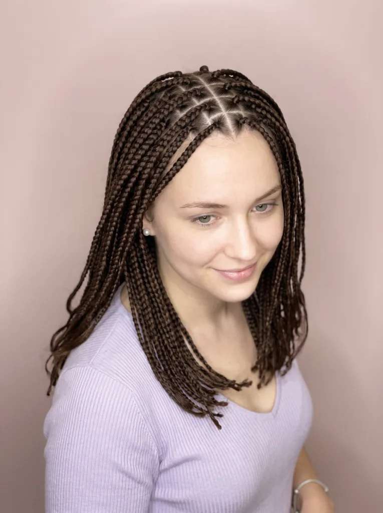 Young woman with dark brown knotless braids and a heart-shaped scalp parting visible at the crown