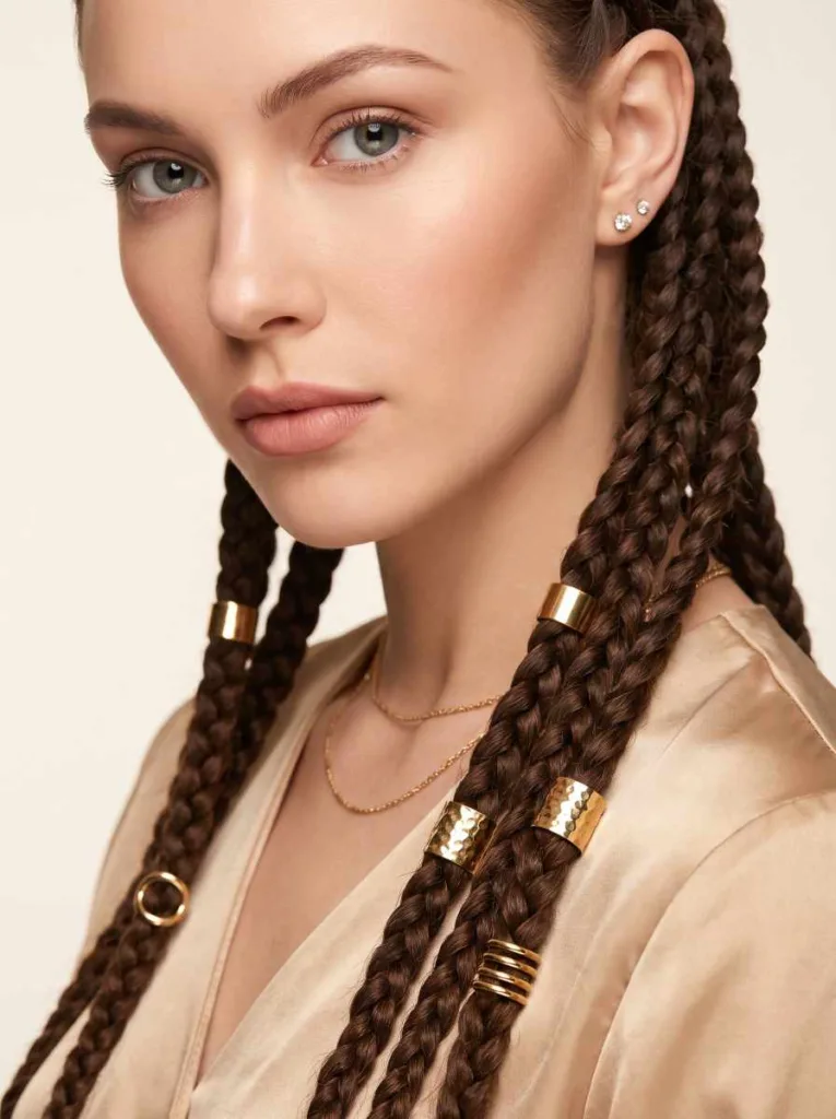 Close-up of dark brown knotless braids with staggered gold hair cuffs glinting under studio light