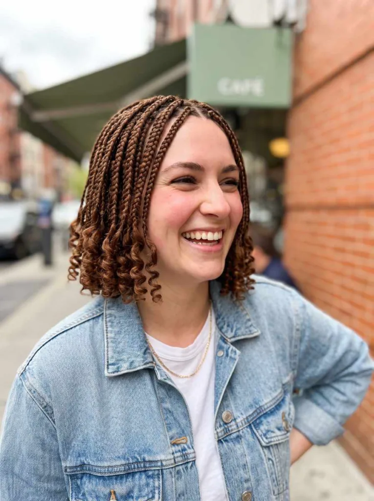 Smiling young woman with short chestnut knotless braids with curly tips above the shoulder