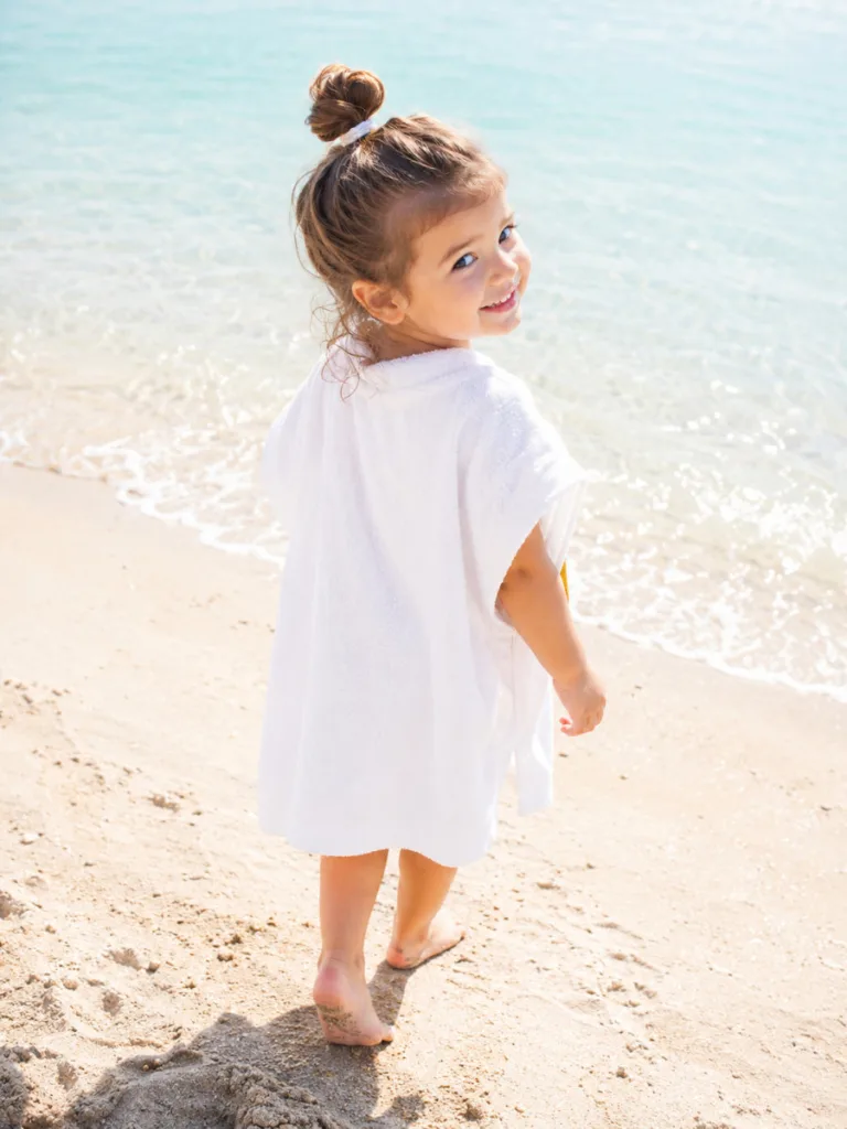 Top knot toddler hairstyle for long hair — summer beach portrait from behind