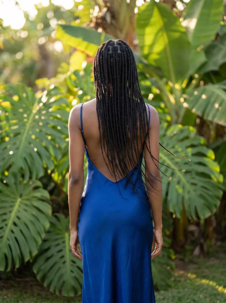 Back view of a slender young woman with hip-length black knotless braids cascading down a cobalt dress