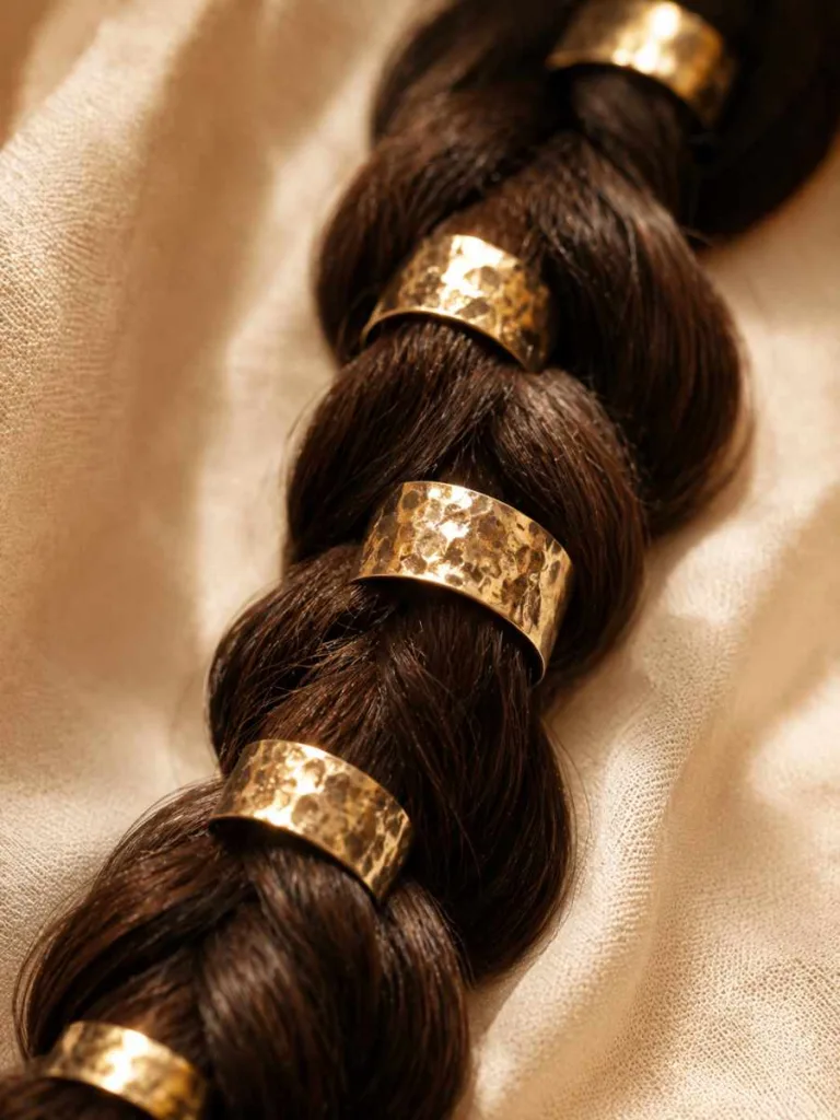 Extreme close-up beauty macro of dark brown dutch braid pigtails with evenly spaced vintage gold hair cuffs, warm studio lighting