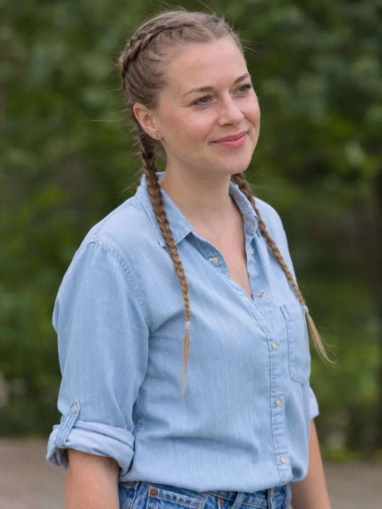Fair-skinned woman with fine light brown hair in double dutch pigtail hairs, outdoor overcast light, soft focus green background