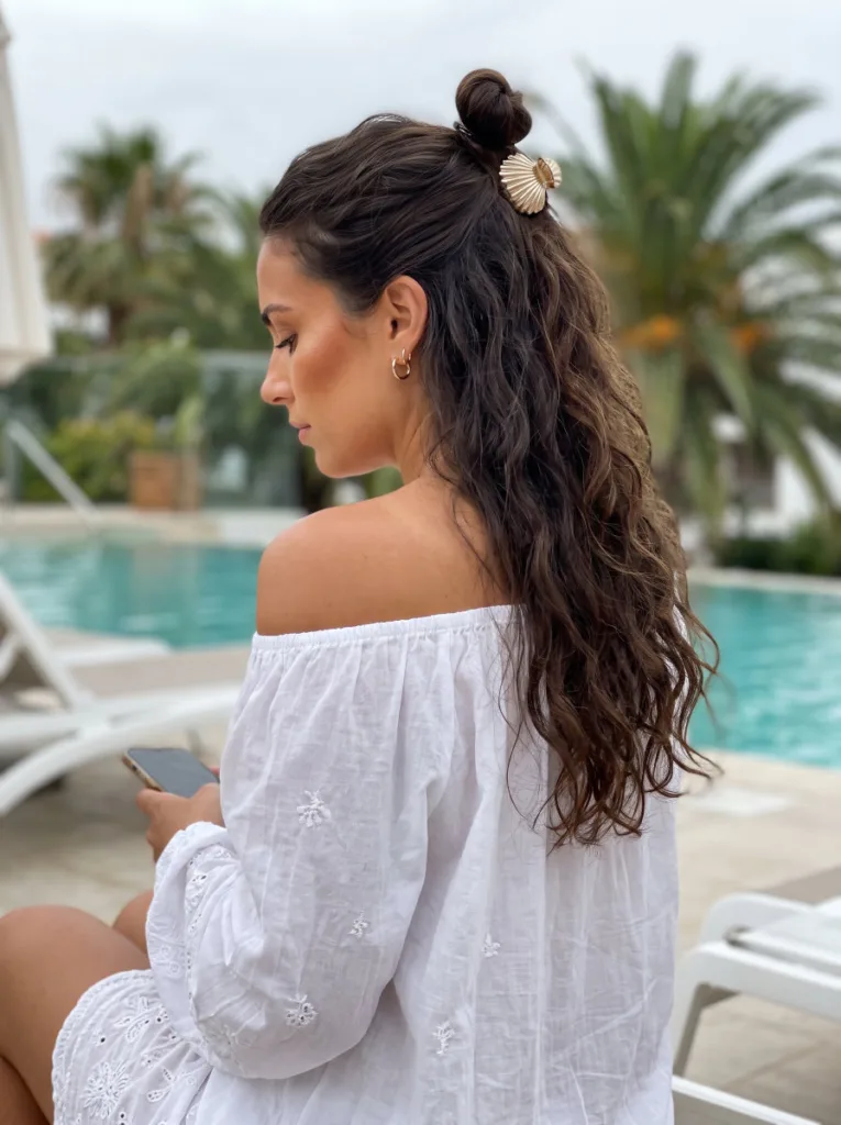 Half-up shell clip vacation bun hairstyle on long dark wavy hair at the beach