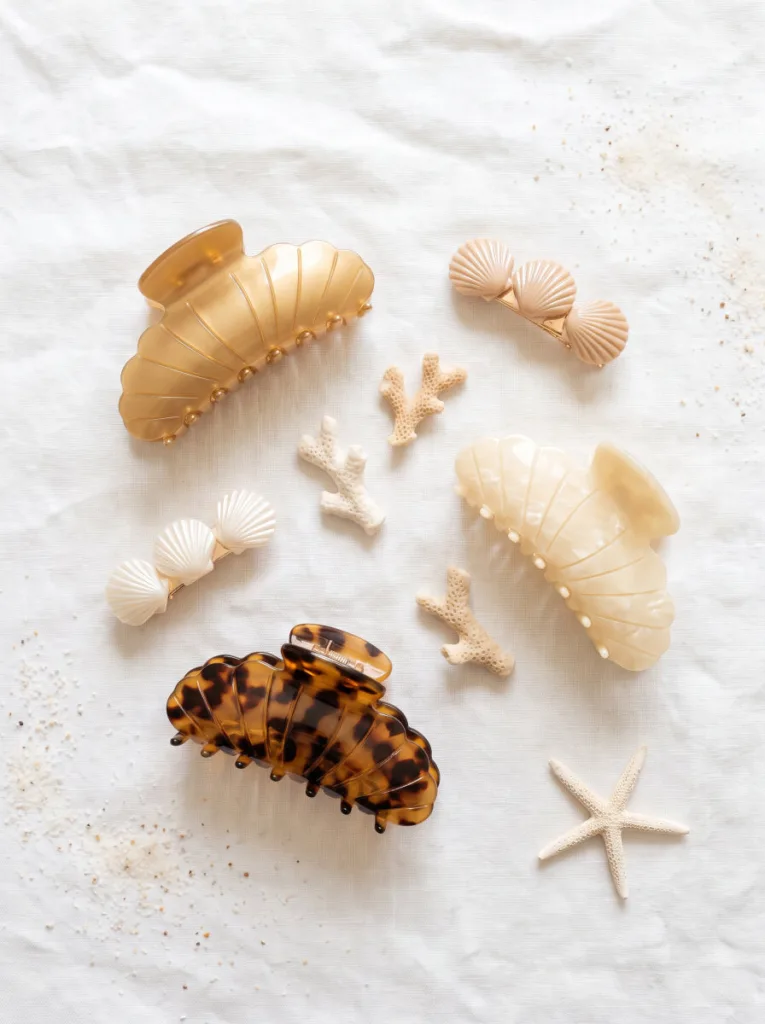 Flat lay of shell hair clips in gold, ivory, and tortoiseshell acetate on white textured linen
