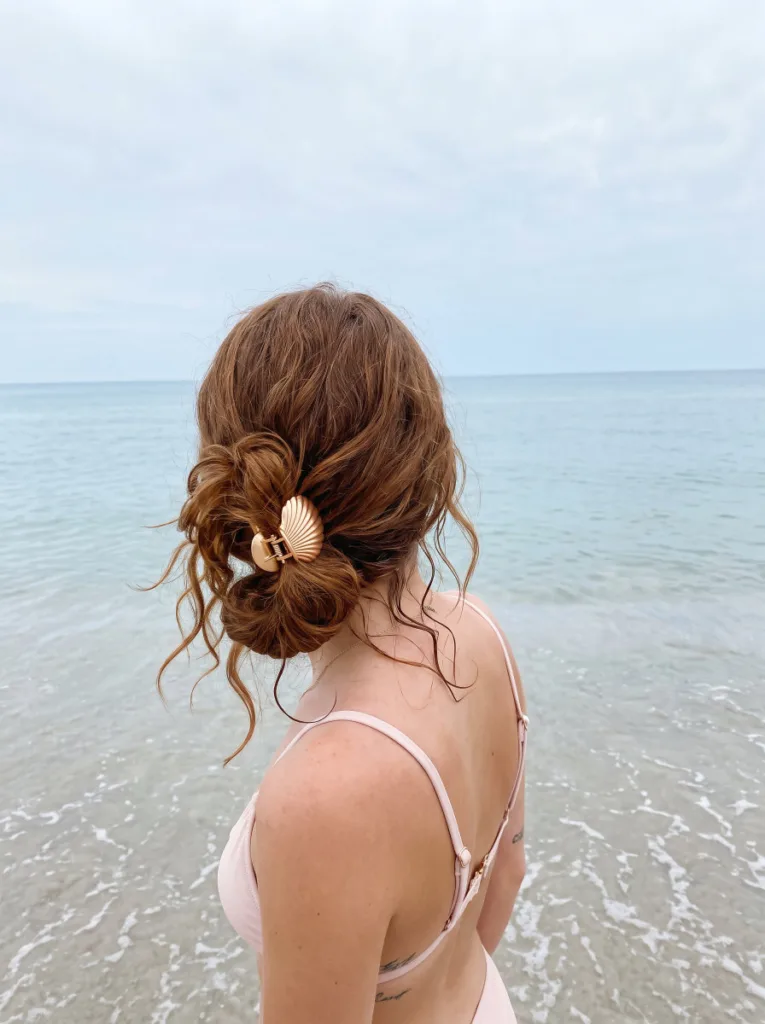 Tousled low shell clip bun on natural wavy hair at the ocean's edge