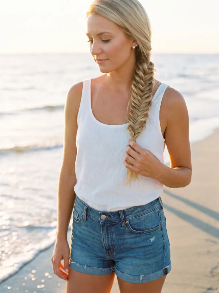 wet-look fishtail braid hairstyle — loose glossy fishtail braid over shoulder on woman at beach water's edge