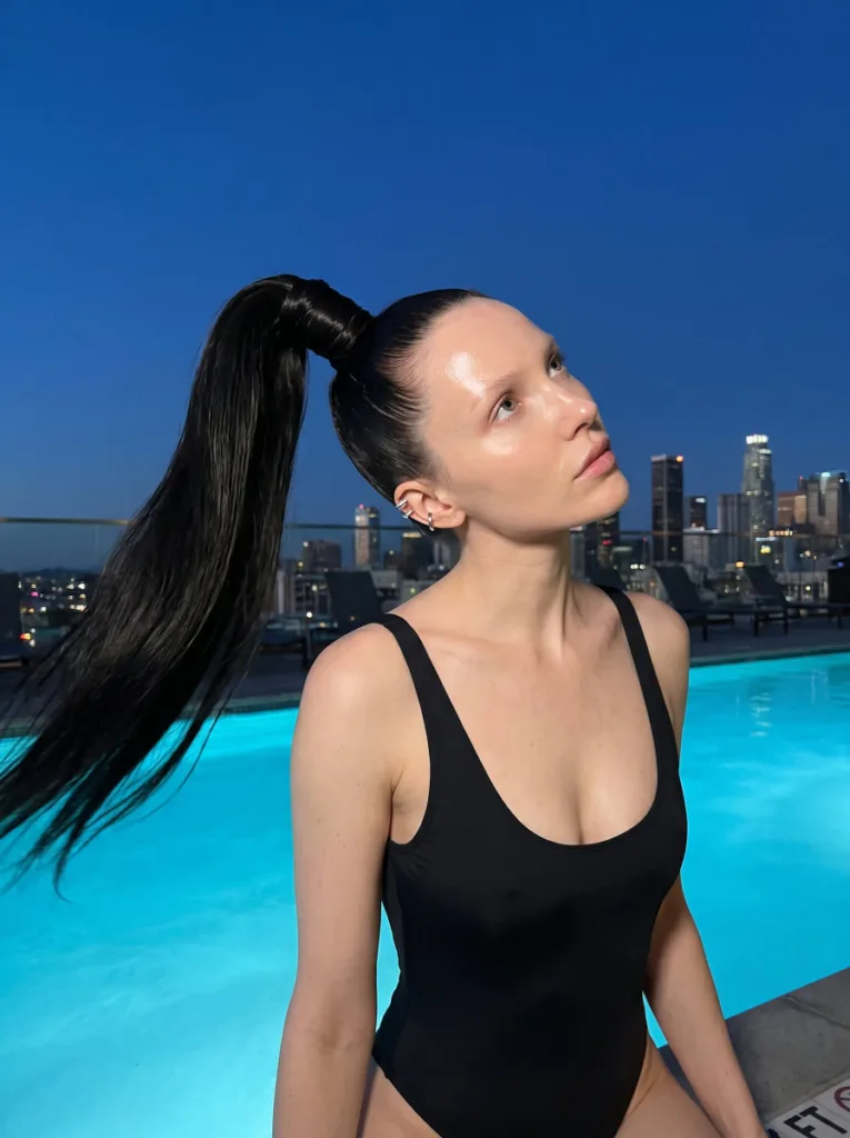 wet-look high ponytail hairstyle on woman at poolside at blue hour — sleek gel-smoothed base with cascading ponytail