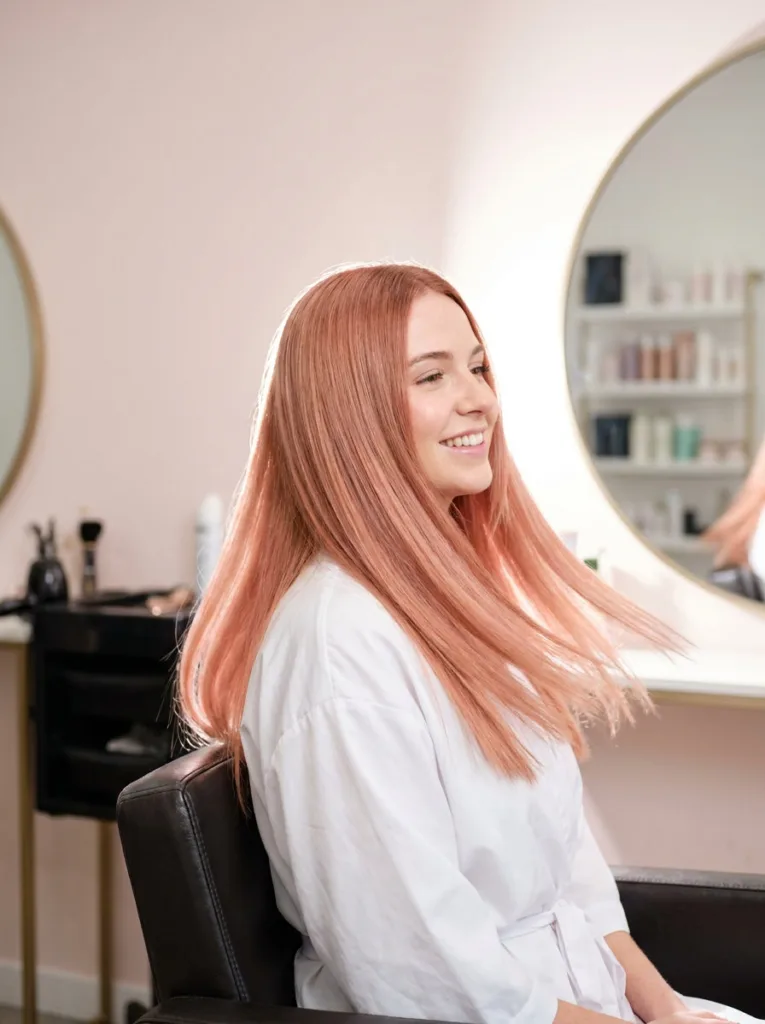 Glossy blush copper hair with a fresh pink-copper demi gloss in a salon chair