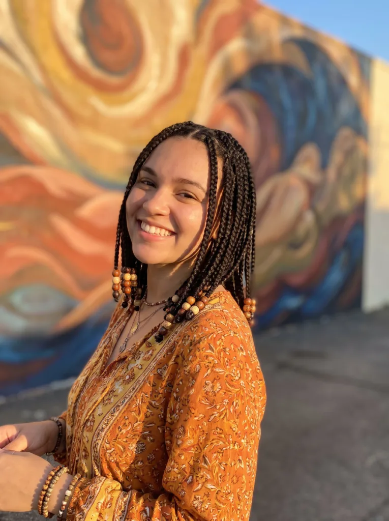 Woman with medium box braids and beaded ends standing in front of a colorful mural