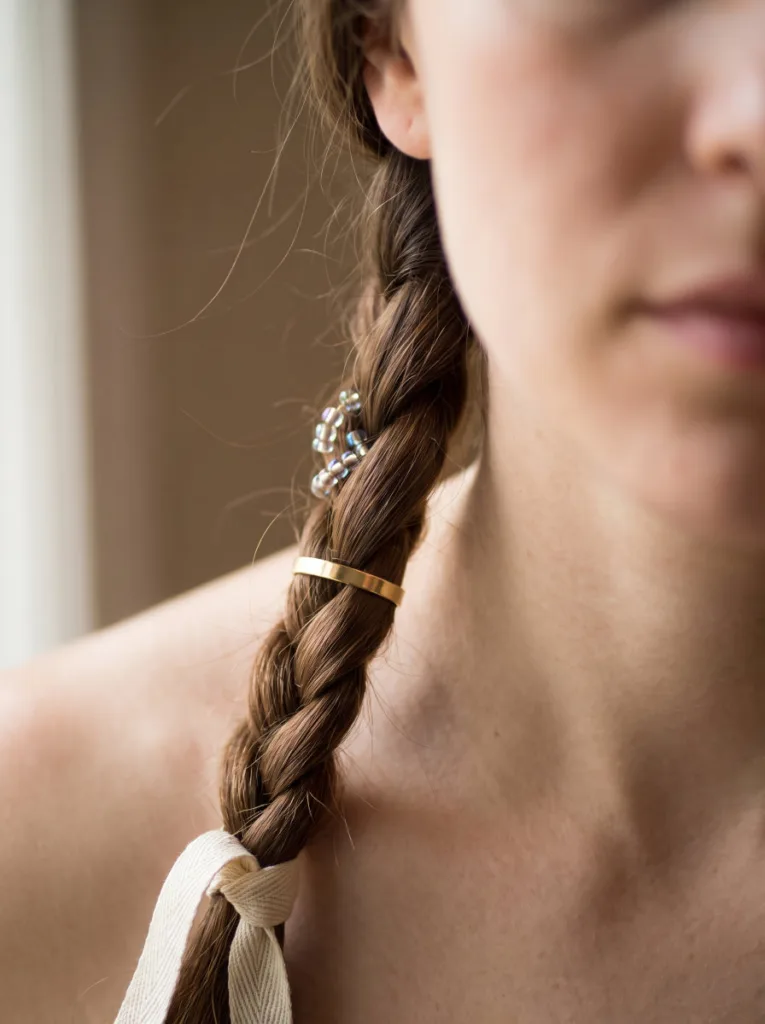 Close-up of a woman's braid decorated with beads, a metal cuff, and a ribbon, showing different boho braid accessories for hair