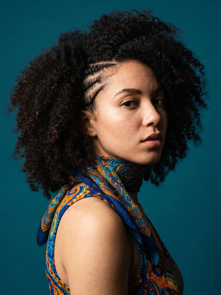 Woman with a cornrowed front section and a bold patterned scarf wrapped around the base of her hair