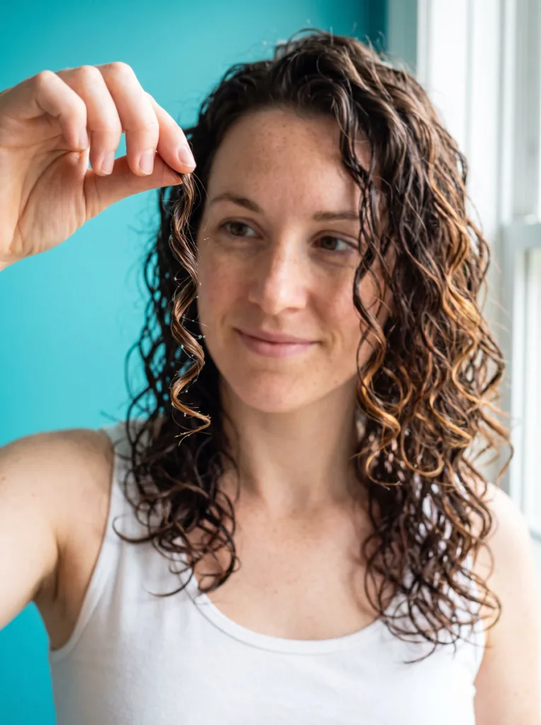 Young woman holding up one wet curl to check her curl type before choosing a protective style