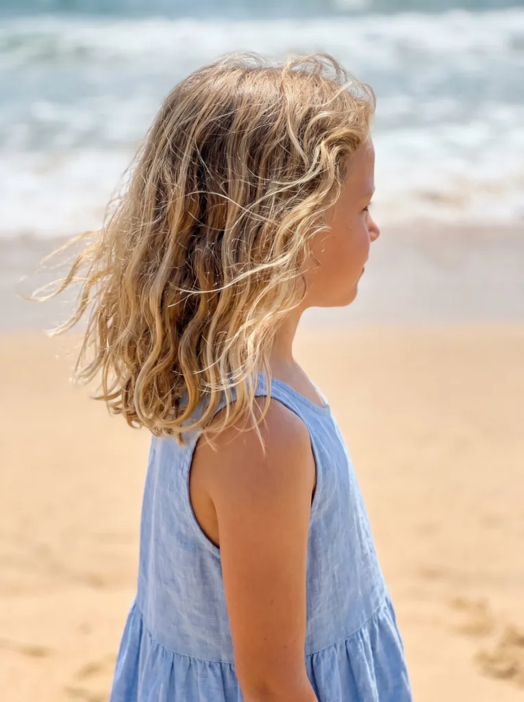 School-age girl with loose beachy waves hairstyle standing on a sandy beach