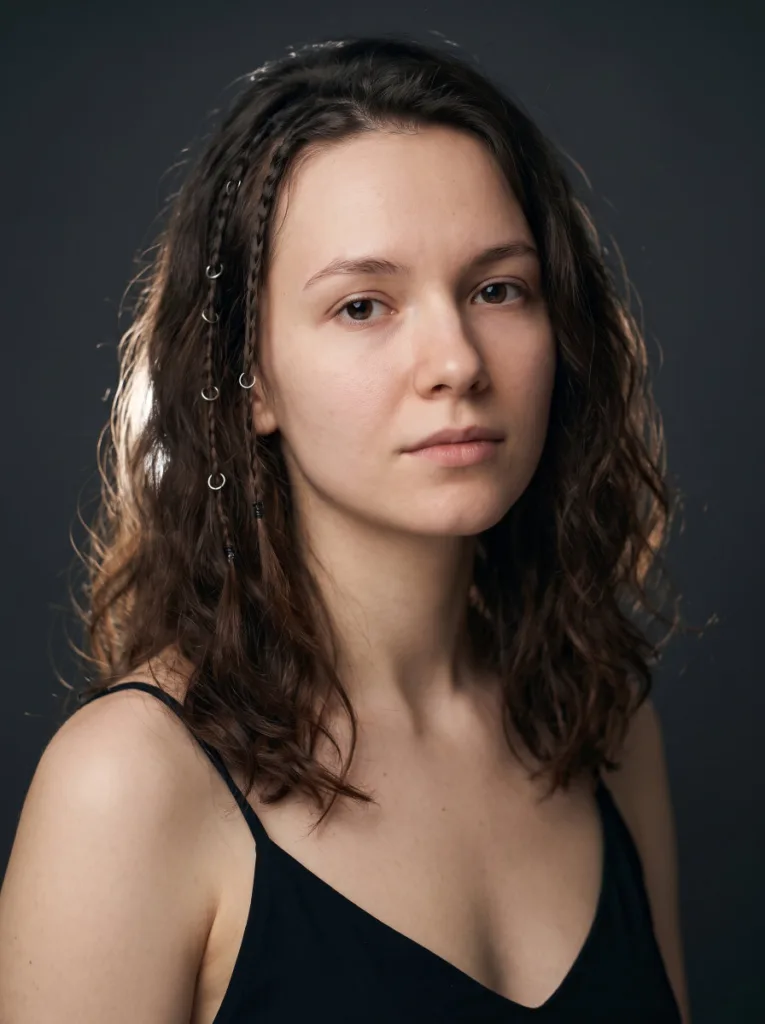 Close-up beauty portrait of a woman with micro accent braids and small silver rings against a dark studio background