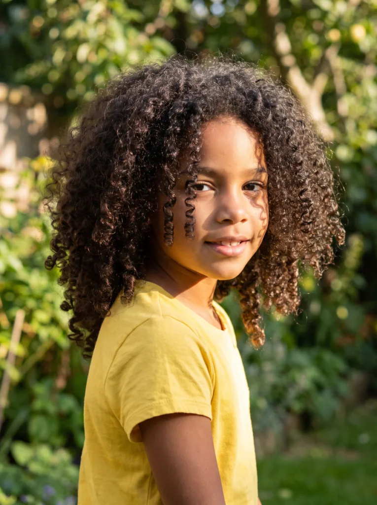 Girl with natural curly hair styled with curl definition in a garden setting
