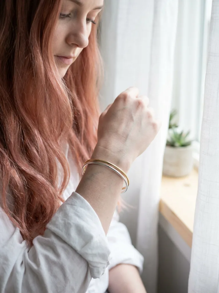 Silver and gold bracelets on a fair wrist to test skin undertone before choosing copper hair