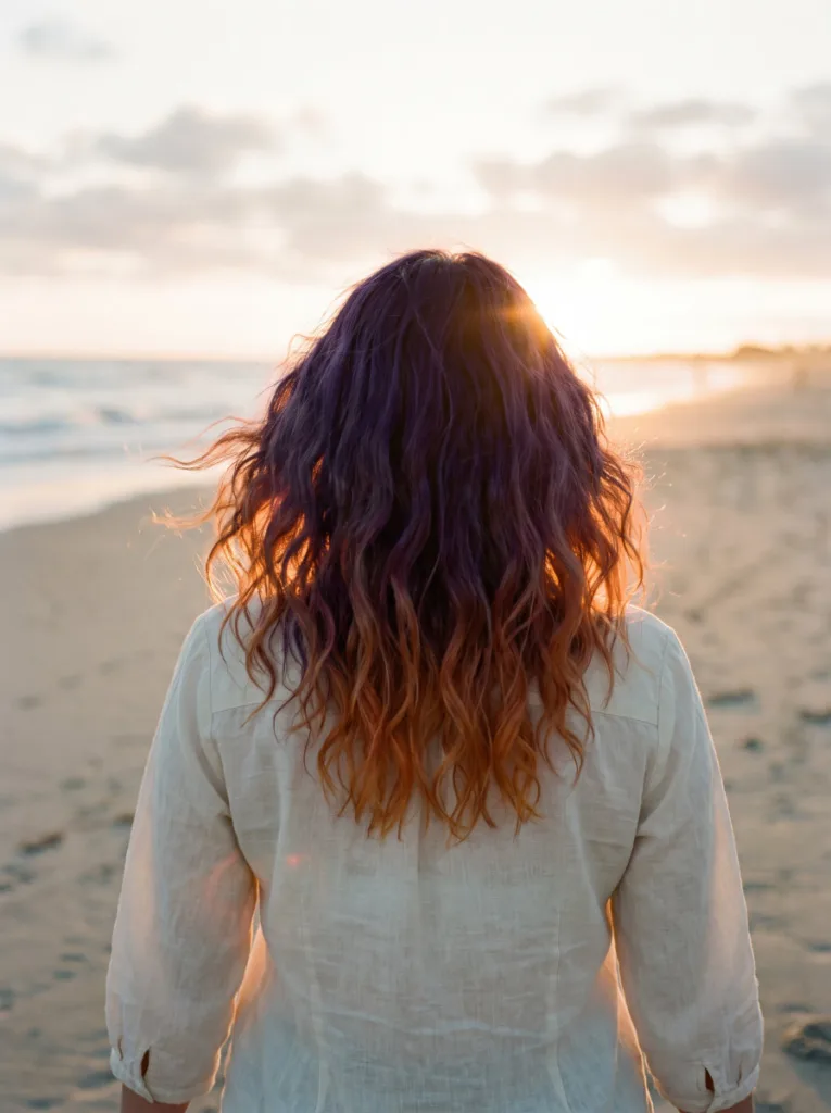 Woman with violet to orange sunset ombre hair color walking on a beach at golden hour