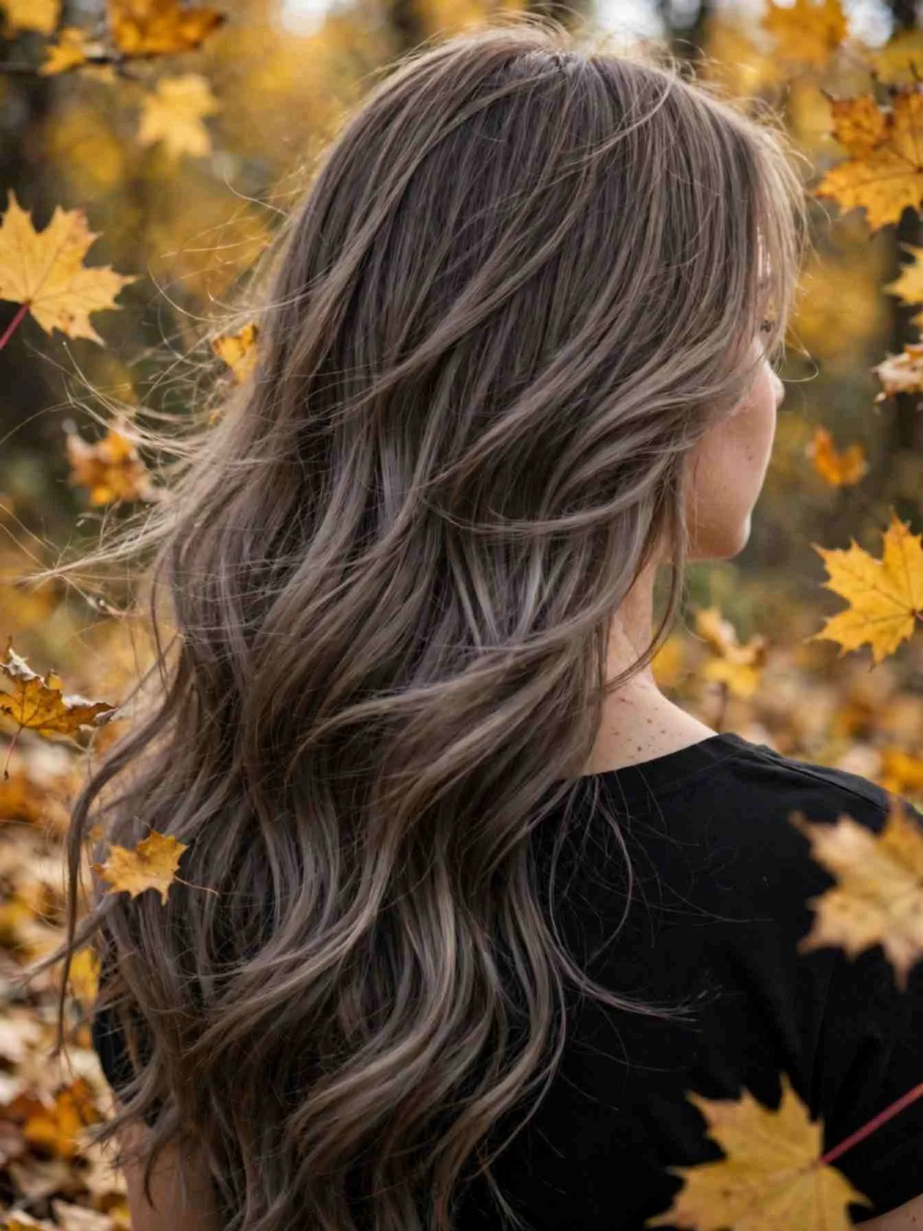 Woman with cool toned fall hair among autumn leaves