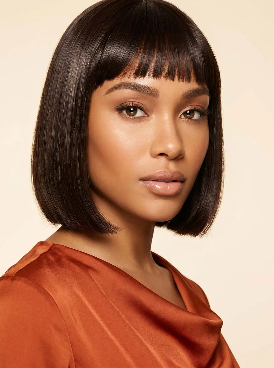 Beautiful woman with classic straight baby bangs and a sleek dark bob, straight-on studio portrait with warm glowing skin