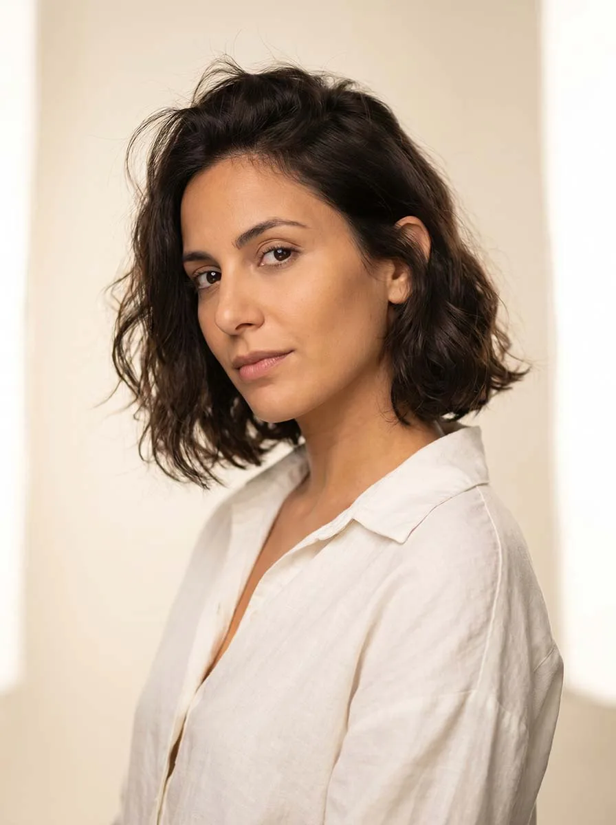 Woman with a classic chin-length wavy bob haircut, soft brunette waves falling at the jaw, photographed in a bright natural light studio